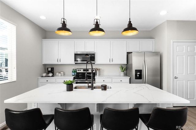 kitchen featuring pendant lighting, a center island with sink, a sink, white cabinetry, and stainless steel appliances