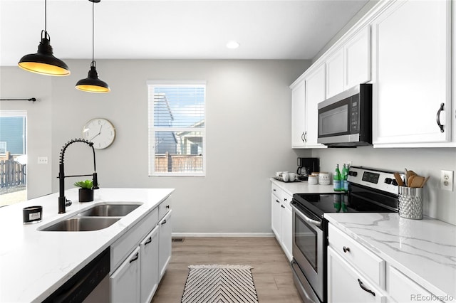 kitchen featuring pendant lighting, light wood-style flooring, stainless steel appliances, white cabinetry, and a sink