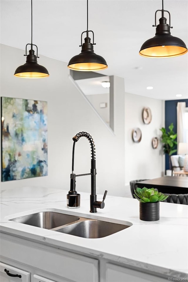 kitchen featuring a sink, light stone countertops, pendant lighting, and white cabinets