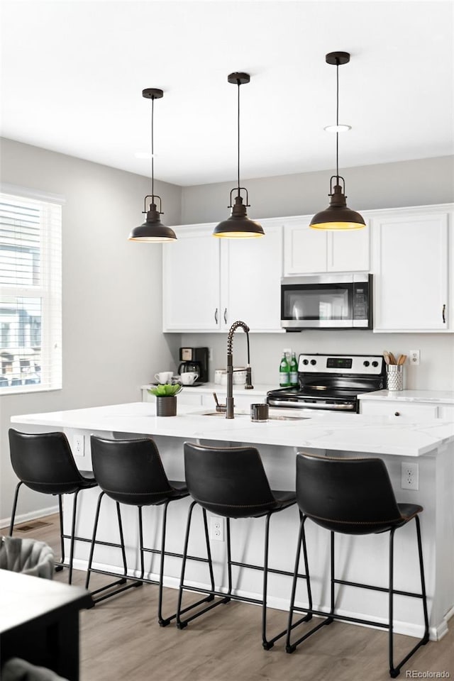 kitchen with wood finished floors, a sink, stainless steel appliances, light countertops, and white cabinetry