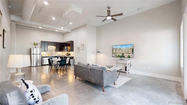 living room with finished concrete flooring, a ceiling fan, a towering ceiling, and baseboards