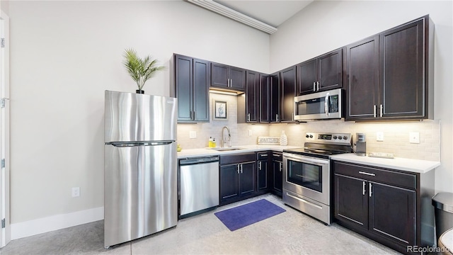 kitchen with stainless steel appliances, a sink, baseboards, light countertops, and tasteful backsplash