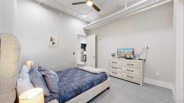 bedroom featuring light wood-style flooring, a high ceiling, baseboards, and a ceiling fan