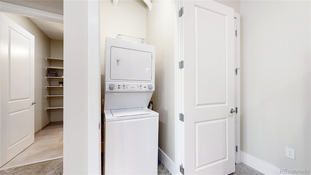 clothes washing area featuring laundry area, baseboards, and stacked washer / dryer