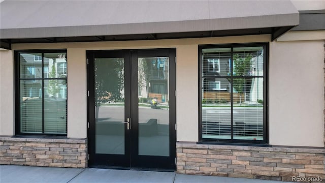 doorway to property with a garage, stone siding, stucco siding, and french doors