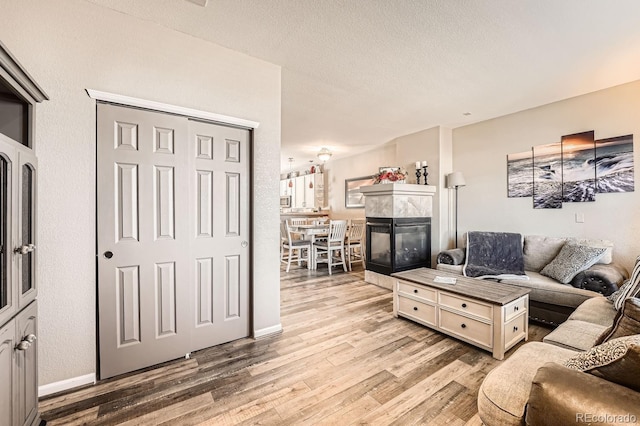 living room with a tile fireplace, baseboards, a textured ceiling, and light wood finished floors