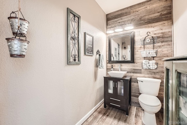 bathroom with wood walls, vanity, toilet, and wood finished floors