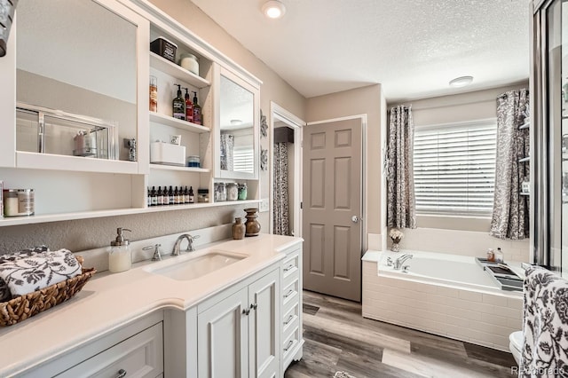 full bath featuring vanity, a textured ceiling, a bath, and wood finished floors