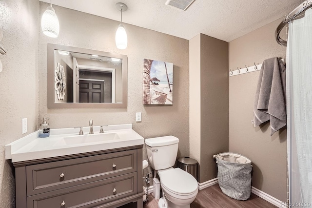 bathroom with visible vents, a textured wall, toilet, wood finished floors, and vanity