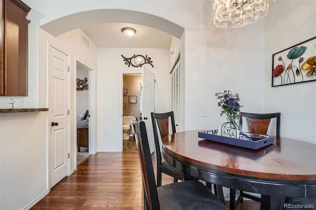 dining area with dark wood-type flooring and an inviting chandelier