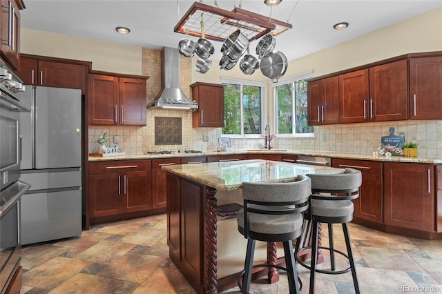 kitchen featuring wall chimney range hood, light stone finish floors, light stone countertops, a sink, and recessed lighting