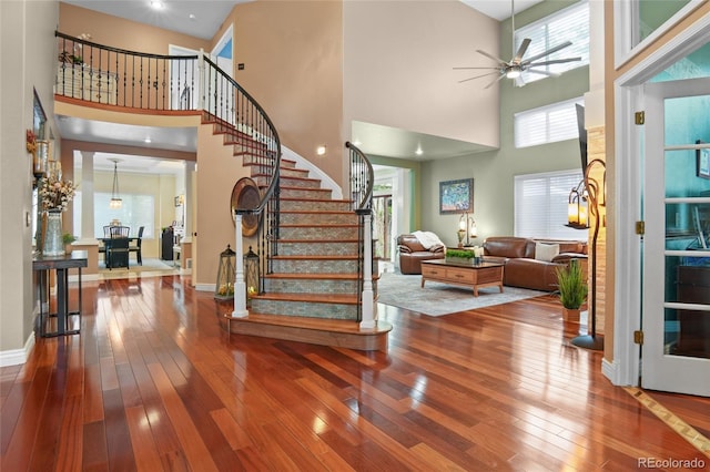 entrance foyer featuring a high ceiling, hardwood / wood-style flooring, stairs, ceiling fan, and baseboards