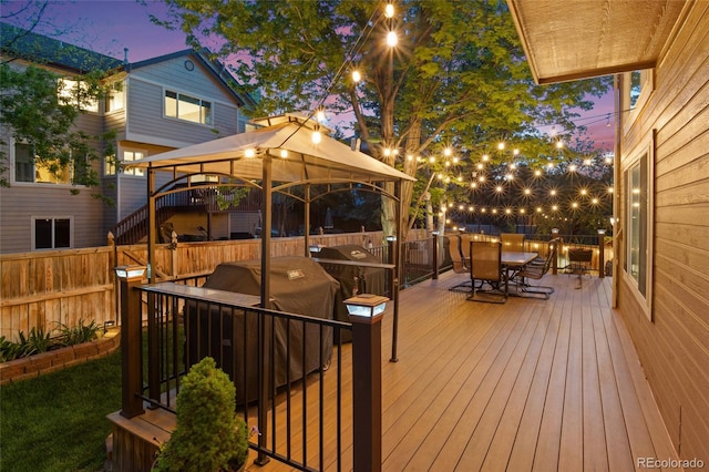 deck at dusk with outdoor dining space, a gazebo, and fence