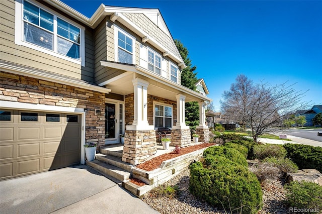 view of front of home with covered porch, stone siding, asphalt driveway, and a garage