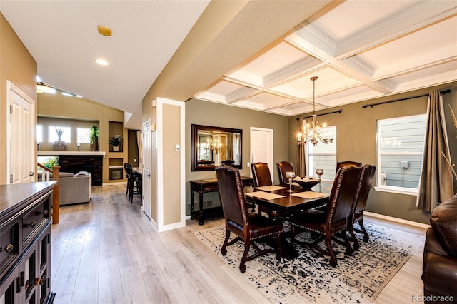dining area featuring a chandelier, baseboards, a fireplace, light wood-style flooring, and beam ceiling