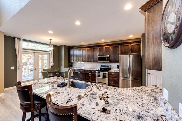 kitchen with stainless steel appliances, french doors, a sink, light stone countertops, and dark brown cabinets