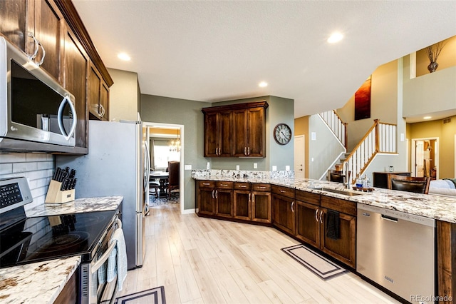kitchen featuring appliances with stainless steel finishes, light wood finished floors, a sink, light stone counters, and recessed lighting