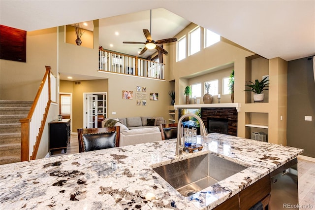 kitchen with a sink, wood finished floors, a ceiling fan, light stone countertops, and baseboards