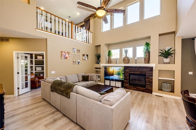 living area with a ceiling fan, light wood-type flooring, a towering ceiling, a fireplace, and built in features