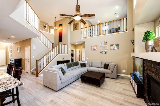 living room with a glass covered fireplace, stairs, wood finished floors, ceiling fan, and baseboards