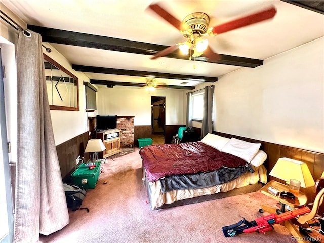 bedroom with wainscoting, carpet floors, wood walls, beamed ceiling, and a ceiling fan