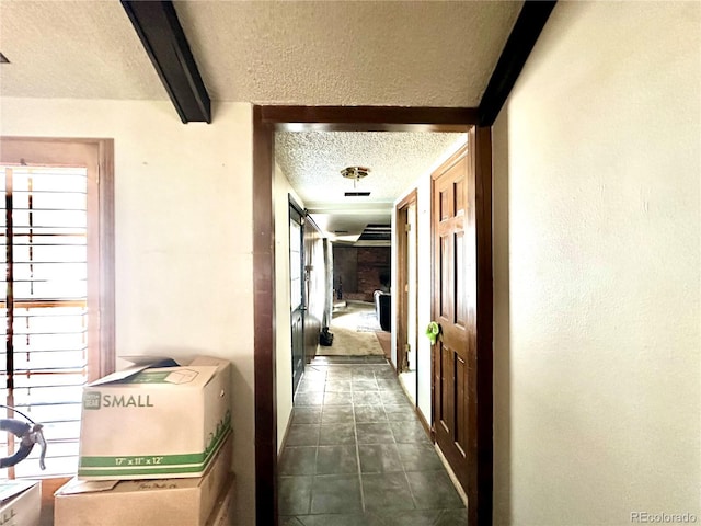 hallway with a textured ceiling, beam ceiling, and dark tile patterned floors