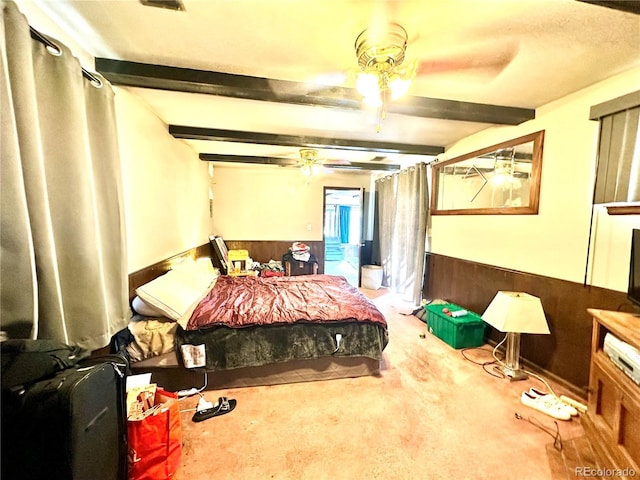 bedroom featuring carpet floors, a wainscoted wall, ceiling fan, and beamed ceiling