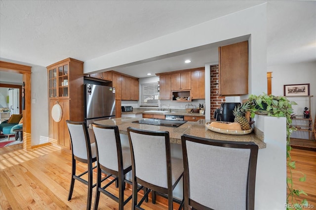 kitchen with stainless steel refrigerator, sink, light hardwood / wood-style flooring, kitchen peninsula, and a textured ceiling