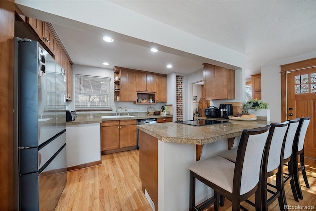 kitchen with black electric stovetop, a breakfast bar, sink, light hardwood / wood-style flooring, and stainless steel refrigerator