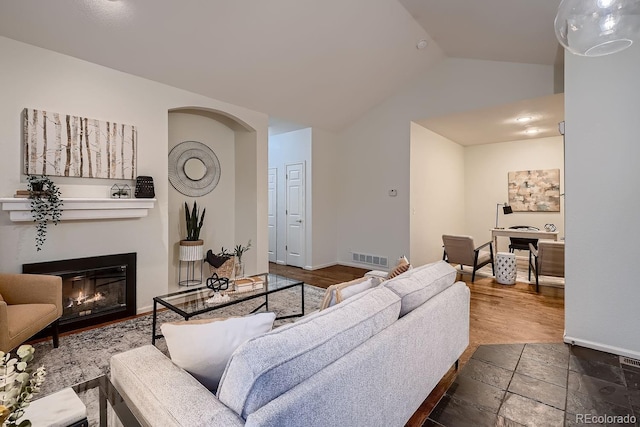 living area with vaulted ceiling, stone tile floors, a glass covered fireplace, and baseboards