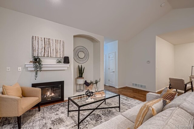 living room with visible vents, a glass covered fireplace, vaulted ceiling, wood finished floors, and baseboards