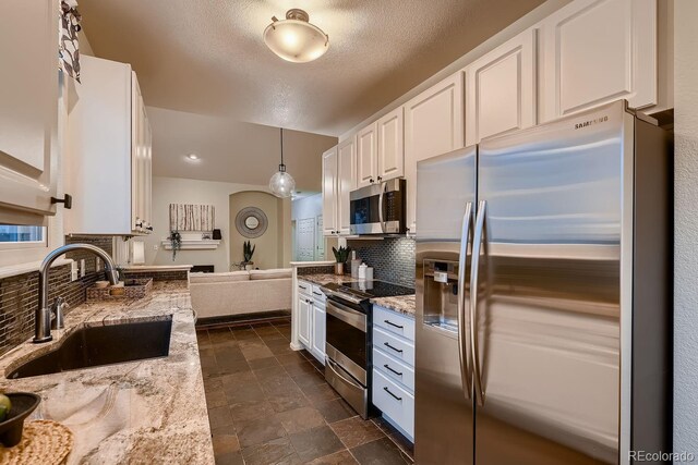 kitchen with stainless steel appliances, hanging light fixtures, a sink, and white cabinetry