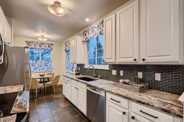 kitchen with stone tile floors, stainless steel appliances, stone countertops, white cabinets, and a sink