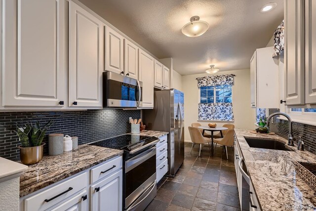 kitchen with stone countertops, appliances with stainless steel finishes, stone tile flooring, white cabinetry, and a sink