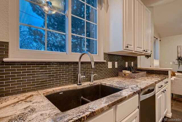 kitchen featuring decorative backsplash, white cabinets, a sink, light stone countertops, and stainless steel dishwasher