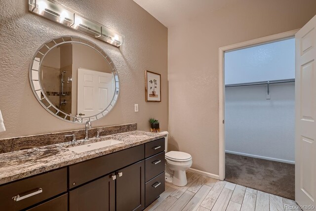 bathroom featuring vanity, baseboards, a spacious closet, wood tiled floor, and an enclosed shower