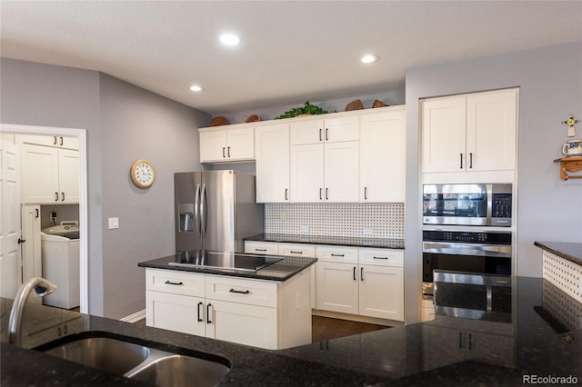 kitchen featuring backsplash, appliances with stainless steel finishes, white cabinetry, a sink, and washer / dryer