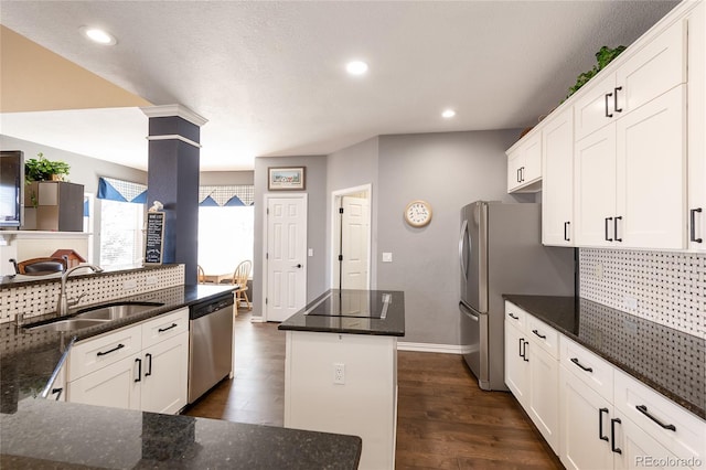 kitchen featuring decorative columns, dark wood-type flooring, a center island, stainless steel appliances, and a sink