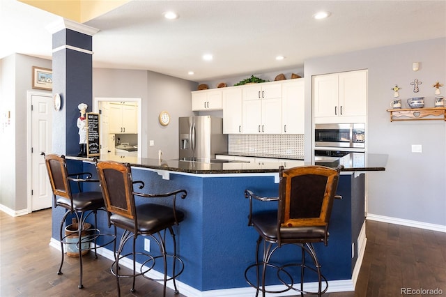 kitchen featuring white cabinets, decorative backsplash, dark wood-style floors, appliances with stainless steel finishes, and a kitchen bar