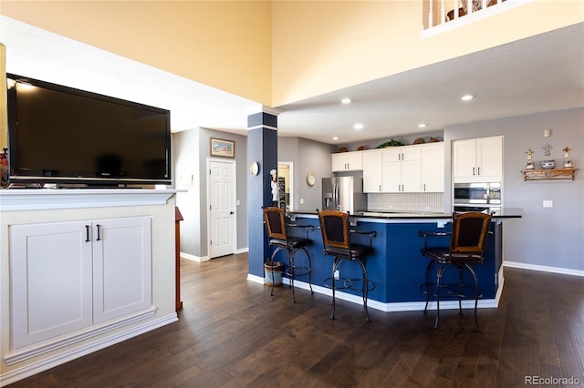kitchen featuring stainless steel appliances, white cabinetry, dark wood finished floors, and a kitchen breakfast bar