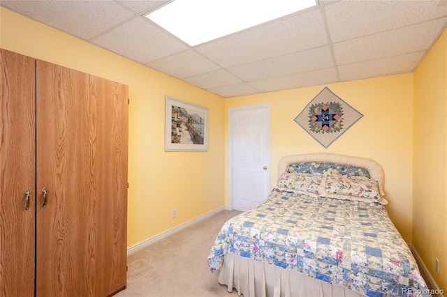 bedroom featuring light colored carpet, a drop ceiling, and baseboards