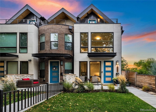contemporary house with brick siding, fence, a front lawn, and stucco siding