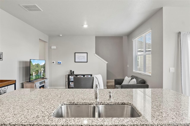 kitchen with light stone counters, sink, and a kitchen island with sink