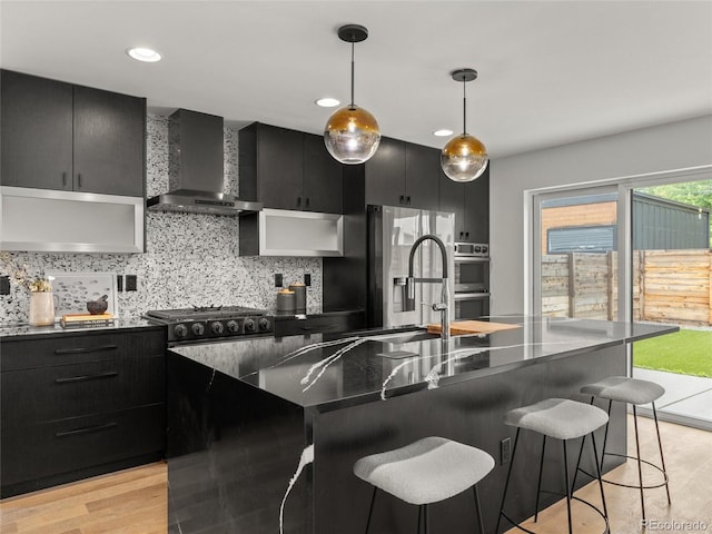 3715 Kalamath St, Denver, CO 80211 - kitchen featuring wall chimney range hood, dark cabinetry, dark countertops, stainless steel appliances, and light wood-type flooring