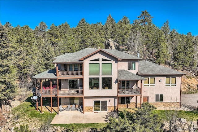 9659 S Turkey Creek Rd, Morrison, CO 80465 - back of property featuring a balcony, a patio area, stucco siding, stone siding, and a shingled roof