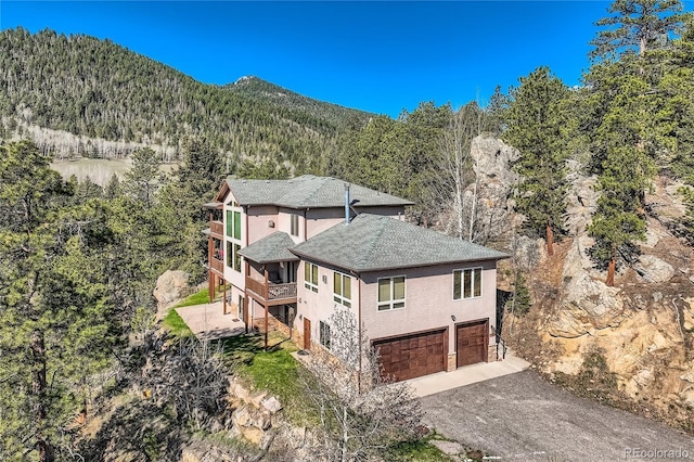 9659 S Turkey Creek Rd, Morrison, CO 80465 - view of home's exterior featuring a garage, a view of trees, driveway, a shingled roof, and stucco siding