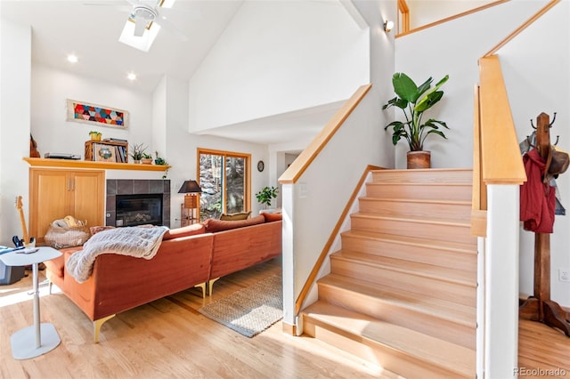 597 Pine Glade Rd, Nederland, CO 80466 - living room featuring stairs, wood finished floors, a tiled fireplace, a ceiling fan, and high vaulted ceiling