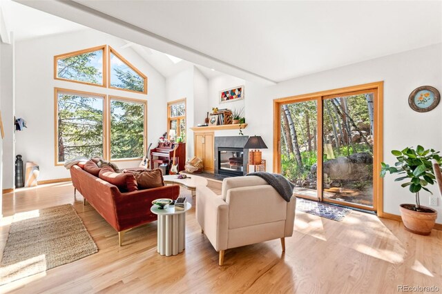 597 Pine Glade Rd, Nederland, CO 80466 - living area featuring a tiled fireplace, light wood-style flooring, baseboards, and high vaulted ceiling