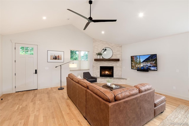 living room with a ceiling fan, baseboards, lofted ceiling, a stone fireplace, and light wood-style floors