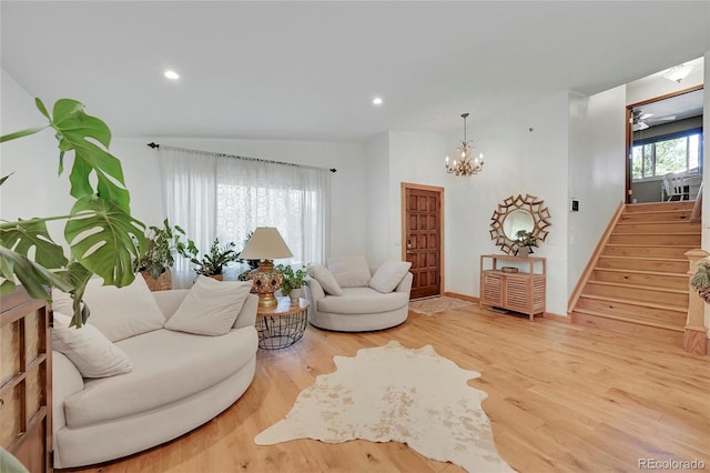 living room featuring ceiling fan with notable chandelier, wood-type flooring, and vaulted ceiling